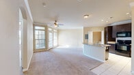 Located at 1240 Riverwalk Terr in Jenks, Oklahoma, this well-appointed one-bedroom, one-bathroom residence offers a thoughtfully designed single-level layout. The open-concept living and kitchen area serves as the heart of the home, bathed in natural light from large multi-pane windows and a set of French doors. Crown molding and a ceiling fan add classic detail to the living space, which features plush wall-to-wall carpeting. The kitchen is equipped with rich dark-walnut cabinetry, granite-look countertops, a tile backsplash, black appliances including a refrigerator and range, and a peninsula with a built-in sink — ideal for casual dining or meal prep. Tile flooring runs throughout the kitchen and entry areas. An elegant arched doorway with pendant lighting connects the living area to the private hallway. The comfortable bedroom includes a ceiling fan, a natural light-filled window, and convenient access to both the bathroom and a dedicated closet. The full bathroom features a tub/shower combination with decorative tile accents, a single vanity, and tile flooring. A dedicated in-unit laundry room with side-by-side washer and dryer completes this efficiently designed home.