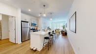 This thoughtfully designed one-bedroom, two-bathroom unit on Diamond Parkway in North Kansas City offers a clean, contemporary aesthetic throughout its efficiently arranged single-floor layout. Light wood-style flooring flows continuously from the open-concept kitchen and living area through the rest of the unit, creating a cohesive and airy feel.

The kitchen serves as a focal point, anchored by a white quartz waterfall island with bar seating and illuminated by globe pendant lights. Gray shaker cabinetry, a subway tile backsplash, and a full suite of stainless steel appliances—including a refrigerator, range, and microwave—complete the space. The adjacent living room receives ample natural light through large windows with horizontal blinds.

The bedroom is a calm, well-proportioned retreat with a window, direct access to a full bathroom, and proximity to an in-unit hallway housing a stacked washer and dryer alongside open closet shelving. Both bathrooms feature gray shaker vanities with white countertops, with one including a tiled tub-shower combination. The overall design is modern and functional, with a neutral white-and-gray palette throughout.