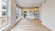 This single-floor unit showcases a clean, contemporary design with light hardwood flooring that flows consistently throughout the space. The open-concept kitchen is well-appointed with light wood cabinetry, a white subway tile backsplash, and a full suite of stainless steel appliances, including a range, built-in microwave, dishwasher, and a French door refrigerator with an ice and water dispenser. A large window adjacent to the kitchen allows generous natural light to fill the living area, with views of the surrounding neighborhood.

The bedrooms are bright and neutrally finished, each benefiting from large windows that frame outdoor greenery and street views. Storage is well-considered, with bedrooms offering dedicated closets — including a walk-in closet with built-in wire shelving and a separate room featuring a sliding-door closet.

The bathroom is finished in a modern style, featuring large-format tile flooring, a tiled shower/tub combination, a light wood vanity with a grey countertop, an undermount sink with matte black fixtures, and a bold black-framed mirror. The overall ambiance is bright, clean, and move-in ready with a cohesive neutral palette throughout.
