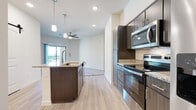 This single-floor residence showcases a modern design with a thoughtful open layout connecting the main living areas. The kitchen serves as the centerpiece, featuring dark wood-toned cabinetry, granite countertops, a subway tile backsplash, and a full suite of stainless steel appliances including an electric range, over-the-range microwave, and a French door refrigerator. A kitchen island with an undermount sink and pendant lighting above adds both function and style, while light wood-look flooring flows throughout the main areas. A sliding barn door adds a contemporary accent near the kitchen corridor.

The living area extends naturally from the kitchen, with ceiling fans providing comfort and a sliding glass door offering access to an outdoor balcony. Bedrooms feature plush carpet, ceiling fans, and windows that bring in natural light, while a generously sized walk-in closet includes wire shelving and a built-in shelf tower for organized storage. Both bathrooms are finished with wood-toned cabinetry, granite countertops, light wood-look flooring, and tub-shower combinations with clean white tile surrounds. A dedicated laundry closet houses a full-size top-load washer and dryer with overhead shelving, adding everyday convenience to this well-designed space.