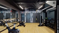 Located at 183 N Addison Ave in Elmhurst, Illinois, this single-floor fitness facility delivers a sleek, modern workout environment designed for both performance and aesthetics. The space features light hardwood-style flooring throughout, which contrasts sharply with the dramatic dark ceiling that showcases exposed ductwork and structural elements — a deliberate industrial design choice that lends the space an energetic, urban character.

The main workout area is well-equipped with Matrix brand stationary cycling bikes, TRX suspension training systems, and an Octagon dumbbell rack, providing a comprehensive range of cardio and strength training options. A dedicated storage zone houses organized racks of medicine balls in various weights, soft dumbbells, plyo boxes, and battle ropes, ensuring all functional fitness tools are neatly accessible.

Large floor-to-ceiling windows along one wall flood the space with abundant natural light and offer open views of the surrounding streetscape, creating an inviting and energizing atmosphere. Full-length mirrors are mounted along interior walls to support proper form and amplify the sense of space. A wall-mounted flat-screen television adds a multimedia element for entertainment or guided workouts.

A bold abstract mural serves as a striking focal point on one wall, adding artistic character to the environment. Linear LED lighting runs across the ceiling, providing bright, even illumination throughout the facility.
