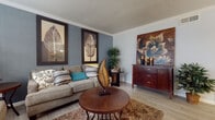 This single-floor residence offers a thoughtfully arranged layout that balances comfort and functionality across several distinct spaces. The living room serves as the heart of the home, featuring light wood-style flooring, crown molding, and a textured ceiling. Cool blue-grey accent walls provide a calming backdrop, complemented by framed botanical artwork and a rich brown area rug that anchors the seating arrangement. Natural light enters through a front-facing window fitted with white blinds.

Adjacent to the living area, a dedicated dining space accommodates a full-sized table and chairs beneath a ceiling-mounted light fixture. A chair rail detail lines the walls, adding a subtle architectural touch to the room.

The galley-style kitchen is efficiently designed, featuring white cabinetry, granite-look countertops, a mosaic tile backsplash, and stainless steel appliances alongside a black refrigerator. The layout maximizes storage and counter space within a streamlined corridor configuration.

The bedroom is a serene retreat with light blue-grey walls, wood-style flooring, and a window providing natural light. A doorway leads directly into the bathroom, which offers a wide vanity with generous cabinet storage below, a large mirror, white upper cabinetry, and bold patterned wallpaper that adds visual interest to the space.