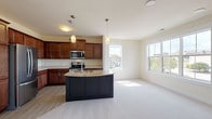 This single-floor home is designed with an open, flowing layout that connects the kitchen and living areas seamlessly. The kitchen is a standout feature, outfitted with rich cherry wood cabinetry extending to the ceiling for ample storage, stainless steel appliances including a refrigerator, microwave, and range, and a large curved island with a granite countertop and integrated sink. Pendant lighting above the island adds a refined touch, while wood-look flooring grounds the cooking space before transitioning to plush neutral carpeting throughout the adjoining living areas.

The spacious living room is anchored by a tile-surround fireplace and benefits from abundant natural light streaming through multiple large windows. Built-in cabinetry provides additional storage and visual interest near the hallway transition. The bedrooms are generously sized, each featuring soft carpeting and large windows that bring in natural light and outdoor views.

The primary bathroom offers a dark wood vanity with a white countertop, tile flooring, a separate shower, and a dedicated walk-in area. A secondary bathroom provides a tub-shower combination, a wood vanity, and light wood-look flooring. Neutral tones and consistent finishes throughout the home create a cohesive and welcoming atmosphere.