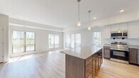 This well-appointed 2-bedroom, 2-bathroom residence in Rosemount, MN offers a thoughtfully designed single-level layout with a bright, open-concept living space. The kitchen serves as a central hub, featuring a large island with granite countertops, white shaker-style cabinetry, stainless steel appliances including a refrigerator, microwave, and range, and elegant pendant lighting. Light wood-tone flooring flows through the kitchen and living area, enhancing the clean, contemporary aesthetic. The living room is generously sized and bathed in natural light from multiple large windows with vertical blinds, offering pleasant outdoor views. Both bedrooms are carpeted for comfort, with the primary bedroom benefiting from its own window with outdoor views. The two bathrooms are finished with granite-topped vanities, tile flooring, and full tub-shower combinations, maintaining a consistent, modern design language. Neutral warm-white walls throughout create a cohesive and inviting atmosphere. The overall layout is efficient and functional, providing comfortable living spaces across the single floor with clear separation between the social and private areas of the home.