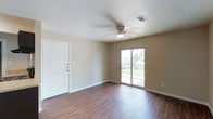 This single-floor unit offers a thoughtfully designed layout with a cohesive blend of practical finishes and comfortable living spaces. The open living area greets you upon entry, showcasing rich, dark hardwood-style flooring that extends throughout the main living spaces, neutral warm-toned walls, and a ceiling fan with integrated lighting. A sliding glass door bathes the room in natural light and provides direct access to a private balcony, offering pleasant outdoor views.

The kitchen is a functional and stylish space featuring dark espresso cabinetry, light granite-style countertops, a double-basin stainless steel sink, and black appliances including a refrigerator, dishwasher, and electric range with an overhead exhaust hood. The continuity of dark hardwood-style flooring ties the kitchen seamlessly to the rest of the living area.

The bedroom is carpeted for added comfort, with a ceiling fan overhead and a window fitted with blinds allowing for natural light and privacy. The bathroom is clean and well-appointed, featuring a tiled soaking tub and shower combination, a dark vanity with a granite-style countertop, and a bright vanity light above the mirror.

An additional living or flex space with matching hardwood-style flooring and neutral walls provides versatile room for various uses. Throughout, the unit maintains a consistent, clean aesthetic with white trim and ample outlet placement.