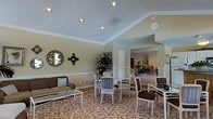Located at 5400 Beverly Hills Dr in Columbus, Ohio, this single-floor space offers a refined and welcoming atmosphere designed for comfort and elegance. The interior is distinguished by soaring vaulted ceilings adorned with recessed lighting, which illuminate the space and create an open, airy feel throughout.

The main lounge area features an ornate, patterned carpet that anchors the room and adds a layer of sophistication to the overall design. Seating is arranged thoughtfully, with a mix of upholstered chairs and a sofa grouped around a glass coffee table, creating an inviting setting for conversation and gathering. Decorative wall accents, including a round mirror and an ornamental wall piece, add character to the soft, neutral-toned walls framed by classic crown molding and wainscoting details.

A wide, open passage connects the primary lounge to an adjoining room, which continues the warm, neutral palette and is furnished with additional seating, suggesting a seamless flow between spaces. Lush indoor greenery adds a natural, refreshing element to the interior. The single-floor layout ensures easy accessibility throughout, while the cohesive décor and architectural details combine to create a polished, comfortable, and functional environment.