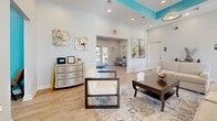 Located at 7466 Stephen Dr in Harrisburg, PA, this single-floor community facility offers a thoughtfully designed layout with a warm, welcoming ambiance throughout. A signature teal and soft blue color palette ties the space together, complemented by light wood-look flooring and an abundance of natural light streaming through multiple windows.

The combined dining, kitchen, and living area serves as the heart of the space. The dining area features a large dark wood communal table with high-back chairs and a wall-mounted TV, ideal for gatherings. Adjacent to it, the kitchen is outfitted with dark cabinetry, stone countertops, and modern appliances, accessible through a convenient pass-through window. The living room area is furnished with comfortable seating, decorative artwork, and elegant accents, creating a relaxed and inviting atmosphere.

The exercise room is generously sized and well-lit, housing multiple treadmills, a stationary bike, a rowing machine, and strength training equipment, all set on durable flooring with a wall-mounted TV for entertainment during workouts.

A private office nook provides a quiet workspace complete with a desk and computer setup. The facility also includes accessible restrooms. Throughout, the consistent use of teal accent walls, recessed lighting, and tasteful décor gives the space a cohesive, polished character.