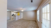 This single-story residence is thoughtfully laid out to maximize functionality and comfort. The spacious living area serves as the heart of the home, featuring neutral-toned carpet, a ceiling fan with integrated lighting, and a textured ceiling. Large windows and a glass-paneled exterior door allow ample natural light to fill the room, while a dedicated entryway provides a welcoming transition into the space.

The galley-style kitchen is efficiently designed with white cabinetry lining both walls, offering generous storage. It is equipped with a full suite of white appliances, including an electric range, refrigerator, built-in microwave, and dishwasher. Light-toned tile flooring and a double stainless steel sink complete the workspace.

The primary bedroom is generously sized, featuring plush carpet, a ceiling fan, and access to both a walk-in closet with built-in shelving and a private en-suite bathroom. The en-suite includes a single vanity with a large mirror, under-sink cabinetry, and a tub-shower combination. A second bedroom offers comparable proportions with carpet, a ceiling fan, and a window with blinds. The second full bathroom mirrors the first in layout and finishes, maintaining a consistent, clean aesthetic throughout.