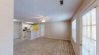 This single-story residence is thoughtfully laid out to maximize functionality and comfort. The spacious living area serves as the heart of the home, featuring neutral-toned carpet, a ceiling fan with integrated lighting, and a textured ceiling. Large windows and a glass-paneled exterior door allow ample natural light to fill the room, while a dedicated entryway provides a welcoming transition into the space.

The galley-style kitchen is efficiently designed with white cabinetry lining both walls, offering generous storage. It is equipped with a full suite of white appliances, including an electric range, refrigerator, built-in microwave, and dishwasher. Light-toned tile flooring and a double stainless steel sink complete the workspace.

The primary bedroom is generously sized, featuring plush carpet, a ceiling fan, and access to both a walk-in closet with built-in shelving and a private en-suite bathroom. The en-suite includes a single vanity with a large mirror, under-sink cabinetry, and a tub-shower combination. A second bedroom offers comparable proportions with carpet, a ceiling fan, and a window with blinds. The second full bathroom mirrors the first in layout and finishes, maintaining a consistent, clean aesthetic throughout.