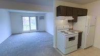 This single-floor unit offers a practical and functional layout centered around an open-concept kitchen and living area. The kitchen is equipped with dark wood cabinetry providing ample storage, a double-basin sink, laminate countertops, a white electric coil-burner range with an overhead exhaust hood, and a dishwasher. The seamless transition into the living area creates a spacious, connected feel ideal for everyday living and entertaining.

The living area is carpeted and generously sized, featuring a ceiling fan with integrated lighting and a wall-mounted air conditioning unit for year-round comfort. A baseboard heater runs along the exterior wall, complementing the climate control options. A large sliding glass door fills the living space with natural light and opens to a private balcony, offering pleasant outdoor views of surrounding greenery.

The neutral color palette throughout — with light walls and beige carpet — gives the space a clean and move-in-ready appearance. Overall, this unit combines straightforward functionality with comfortable living essentials, making it a practical choice for those seeking a well-equipped, easy-to-maintain space.