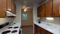 Located at 714 Riverside Drive in Salisbury, Maryland, this single-floor residence offers a practical and comfortable living environment. The kitchen is a standout feature, thoughtfully designed with rich, warm-toned wood cabinetry that provides generous storage above and below the countertops. A clean, white sink sits beneath the cabinetry, complemented by a white electric range, making the space both functional and easy to maintain. The kitchen's layout follows a galley-style configuration, allowing for efficient use of space while maintaining an open sightline into the adjacent area. A ceiling fan overhead ensures comfortable airflow throughout. Natural light filters in through a window that frames a view of surrounding greenery, bringing a touch of the outdoors inside and adding brightness to the interior. The flooring transitions from the kitchen into a carpeted area, adding warmth underfoot in the connected living space. The overall ambiance of the home is cozy and practical, with a neutral color palette that provides a welcoming, move-in-ready feel. The residence is ideally positioned in Salisbury, a city known for its riverside character and community-oriented neighborhoods.