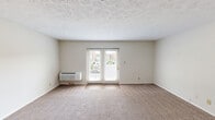 Located at Poplar Level Plaza in Louisville, Kentucky, this efficiently designed single-floor unit makes thoughtful use of its space across a kitchen, bathroom, hallway, closet, and open living area. The main living space features neutral-toned wall-to-wall carpeting, a textured ceiling, and a wall-mounted HVAC unit. A set of French doors floods the room with natural light and provides direct access to a private balcony, offering outdoor views of the surrounding area. The kitchen is well-appointed with white shaker-style cabinetry, granite-look countertops, a stainless steel sink, a stainless steel refrigerator, and an electric range. Wood-look flooring in the kitchen adds a clean, modern contrast to the carpeted living area. The bathroom includes a full tub-shower combination with floor-to-ceiling tile surround in a warm earth tone, a granite-look vanity countertop, wood-look flooring, and chrome fixtures including a grab bar for added accessibility. A hallway connects the rooms with a dedicated closet providing practical storage. The overall aesthetic is clean and neutral, with a straightforward layout that maximizes functionality throughout.