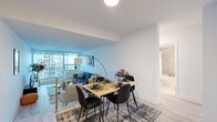 This thoughtfully designed 2-bedroom, 1-bathroom unit offers a functional and modern layout across a single floor. Light wood-toned flooring runs throughout, complementing the crisp white walls and creating a clean, cohesive aesthetic.

The open-concept living and dining area serves as the heart of the unit. Floor-to-ceiling windows flood the space with natural light and frame urban city views, with access to a private balcony from the living room. The dining area comfortably accommodates a full-sized table and chairs, making it ideal for everyday meals or entertaining.

The kitchen features an L-shaped layout with white cabinetry extending to the ceiling for ample storage, a full suite of stainless steel appliances including a refrigerator, electric range, microwave, and dishwasher, as well as recessed lighting and light flooring that ties seamlessly into the rest of the unit.

The spacious primary bedroom is filled with natural light from a wide window overlooking surrounding buildings and offers generous room for a queen or king-sized bed alongside additional furnishings. The second bedroom is well-proportioned and similarly bright.

The bathroom includes a full bathtub with a shower, finished with large-format neutral tiles for a clean, contemporary look. A hallway connects all rooms efficiently, completing this well-organized and stylish urban home.