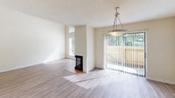 This two-story home offers a well-organized layout with distinct living areas spread across both levels. The main living and dining area is a bright, open space highlighted by wood-style laminate flooring and abundant natural light streaming through large sliding glass doors that overlook an outdoor area. A freestanding corner fireplace with a tiled hearth serves as a central focal point, adding both character and warmth to the room. A pendant light fixture anchors the dining area, and the textured ceiling is consistent throughout the home.

The kitchen is efficiently designed with ample white raised-panel cabinetry providing generous storage. Light-toned countertops offer functional workspace, and appliances include a stainless electric range with an overhead ventilation hood and a black dishwasher. A double-basin sink is positioned beneath a window, allowing natural light into the space. Wood-style flooring continues through the kitchen, maintaining a cohesive look.

The bedrooms feature neutral-toned carpet, white walls, and windows fitted with horizontal blinds, ensuring both comfort and privacy. Each room includes floor-level HVAC vents for climate control. Throughout the home, a clean, neutral color palette creates a bright and versatile atmosphere suitable for a variety of furnishing styles.