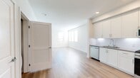 This 670-square-foot, one-bedroom, one-bathroom ground-floor apartment at 30950 Hanover Ln, Unit 01-103, in Menifee, CA offers a clean, modern design throughout. The open-concept kitchen and living area features light wood-look luxury vinyl plank flooring, recessed lighting, and multiple windows fitted with white horizontal blinds that allow abundant natural light. The kitchen is well-appointed with white shaker-style cabinetry, gray quartz countertops, a white subway tile backsplash, and a full suite of stainless steel appliances including a gas range, over-the-range microwave, dishwasher, and refrigerator. The living area includes a glass-paneled exterior door providing additional natural light and outdoor access. The primary bedroom measures 140 square feet and is carpeted, featuring a window with outdoor views and direct access to a dedicated walk-in closet equipped with wire shelving and hanging rods on two walls. The bathroom offers a full-size soaking tub with a combination shower, white tile surround, a white vanity with gray countertop, and wood-look flooring. The unit's neutral color palette and contemporary finishes create a bright, functional living environment.