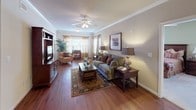 This well-appointed 2-bedroom, 2-bathroom residence offers a thoughtful single-level layout designed for comfortable everyday living. The living room serves as the heart of the home, showcasing rich hardwood flooring, crown molding, a ceiling fan, and large windows dressed with warm drapery that invite abundant natural light. Adjacent to the living area, a dedicated dining space features hardwood floors and an elegant chandelier overhead, providing an inviting setting for meals.

The kitchen is a standout, equipped with dark espresso cabinetry, dark granite countertops, a tile backsplash, and black appliances including a range and refrigerator. A breakfast bar with seating adds a casual dining option and connects seamlessly to the main living areas.

Both bedrooms offer plush carpeting, ceiling fans, and natural light from well-placed windows. The primary bedroom is generously sized with ample closet space. Each bathroom is neatly finished with a vanity, tub-shower combination, and hardwood flooring, with one bathroom featuring a walk-in closet conveniently located nearby.

Throughout the residence, warm neutral tones, crown molding accents, and consistent hardwood flooring in the main areas create a cohesive and inviting atmosphere suited for a range of lifestyles.