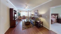 This well-appointed 2-bedroom, 2-bathroom residence offers a thoughtful single-level layout designed for comfortable everyday living. The living room serves as the heart of the home, showcasing rich hardwood flooring, crown molding, a ceiling fan, and large windows dressed with warm drapery that invite abundant natural light. Adjacent to the living area, a dedicated dining space features hardwood floors and an elegant chandelier overhead, providing an inviting setting for meals.

The kitchen is a standout, equipped with dark espresso cabinetry, dark granite countertops, a tile backsplash, and black appliances including a range and refrigerator. A breakfast bar with seating adds a casual dining option and connects seamlessly to the main living areas.

Both bedrooms offer plush carpeting, ceiling fans, and natural light from well-placed windows. The primary bedroom is generously sized with ample closet space. Each bathroom is neatly finished with a vanity, tub-shower combination, and hardwood flooring, with one bathroom featuring a walk-in closet conveniently located nearby.

Throughout the residence, warm neutral tones, crown molding accents, and consistent hardwood flooring in the main areas create a cohesive and inviting atmosphere suited for a range of lifestyles.