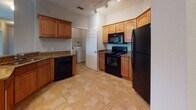 This single-floor residence is designed with an open-concept layout that seamlessly connects the kitchen and living areas. The kitchen is well-appointed with warm honey-toned cabinetry, granite countertops, and a full suite of black appliances, including a refrigerator, range, microwave, and dishwasher. A curved peninsula with an undermount sink serves as a natural divider between the kitchen and the carpeted living area, which benefits from multiple windows fitted with blinds and a ceiling fan. Vertical blinds cover a sliding door, allowing for natural light control. Track lighting illuminates both the kitchen and adjoining spaces effectively.

The entry foyer features tile flooring and provides access to a closet. A dedicated laundry area with a washer and dryer is conveniently located off the kitchen. The bedrooms are carpeted and include closets with bifold doors and ceiling fans. Two bathrooms echo the home's design language with granite-topped vanities, warm wood cabinetry, and tile flooring. One bathroom features a tub-shower combination with tile surround, while the other includes a walk-in shower with a sliding glass door. Overall, the space presents a cohesive, functional interior with consistent finishes throughout.