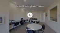 Located at 28155 Encanto Drive in Menifee, California, this single-floor community amenity space is thoughtfully designed to serve as a social and recreational hub. The layout encompasses two distinct areas — a living room and a game room — each offering a unique environment for relaxation and entertainment.

The living room area features warm, neutral-toned walls, recessed lighting, and plush carpeted flooring throughout. Multiple round white tables with sleek black chairs are arranged to encourage casual gatherings, while a leather sofa provides comfortable seating. A dedicated workstation along one wall offers computer access, and framed artwork adds a decorative touch. Large glass-panel doors along one side allow natural light to filter in and provide a connection to the outdoors.

The game room is a standout feature, centered around a full-size billiards table with a classic red felt surface and a vintage-style green pendant light fixture overhead. A wall-mounted flat-screen TV and a cue rack complete the setup. Interior windows connect the game room visually to the living area, creating an open and cohesive feel.

A separate lounge nook showcases a large sectional sofa adorned with framed classic movie posters, a wall-mounted TV, and a media console, creating a cozy cinema-inspired retreat within the space.