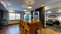 Located at 1202 Crescent Dr in Tarrytown, NY, this single-floor leasing and amenity space delivers a striking blend of mid-century modern aesthetics and contemporary design. The welcoming entrance features a sculptural marble-top tulip table, a multi-globe chandelier, and black-framed glass doors that flood the space with natural light and views of the surrounding neighborhood. Rich hardwood flooring flows throughout, anchoring the cohesive design language.

The leasing office area includes a substantial walnut desk paired with a teal upholstered chair, patterned area rugs in teal and gold tones, and curated abstract wall art. A broad window frames outdoor greenery, lending the workspace an open, inviting feel.

A communal lounge area features an oversized charcoal sectional sofa adorned with teal, yellow, and patterned throw pillows, tufted leather ottomans, and bold large-scale graphic artwork. Pendant lighting completes the sophisticated yet relaxed atmosphere.

The dining and collaboration zone centers on a warm walnut communal table with mustard-yellow chairs, complemented by pendant dome fixtures and a dramatic dark-framed accent wall showcasing geometric art. Vibrant pops of yellow, teal, and blue are woven consistently throughout the space via furnishings and décor, creating an energetic yet polished environment ideal for both professional interactions and community gatherings.