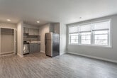 Located at 205 34th St. in Virginia Beach, Virginia, this single-floor unit offers a clean, contemporary design throughout. The open living area is finished with light-toned wood-look flooring and neutral gray walls, creating a bright and versatile space. Large windows fitted with horizontal blinds invite generous natural light and frame views of the surrounding Virginia Beach cityscape.

The kitchen is efficiently designed and features gray cabinetry, a horizontal tile backsplash, light countertops, and a full suite of stainless steel appliances including a refrigerator, range, and dishwasher. The layout allows for a seamless flow between the kitchen and the living area.

The bedroom is a well-proportioned, quiet retreat with the same wood-look flooring, soft gray walls, and a mirrored bifold closet that maximizes storage. A window in the bedroom provides additional natural light and urban views.

The bathroom is finished with large-format marble-look tile covering both the floor and the full shower surround, giving the space a clean, upscale aesthetic. A walk-in style shower with brushed nickel fixtures completes the room. Throughout the unit, the consistent use of neutral tones, modern fixtures, and quality finishes creates a cohesive and move-in-ready living environment.