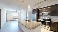 Located at 3033 Ohio Dr in Frisco, TX, this 2-bedroom, 2-bathroom residence offers a thoughtfully designed single-floor layout with modern finishes throughout. The open-concept living and kitchen area serves as the heart of the home, featuring light wood-style flooring, recessed lighting, and a ceiling fan that enhances the airy atmosphere. The kitchen is a standout, equipped with a large granite-topped island with an undermount sink, sleek pendant lighting, dark espresso cabinetry, subway tile backsplash, stainless steel appliances including a refrigerator, microwave, and range, and track lighting overhead. Natural light filters in through windows at the far end of the living area, creating a bright and welcoming ambiance. Both bedrooms are carpeted and offer a comfortable, quiet retreat, with the primary bedroom featuring a ceiling fan and a dedicated walk-in closet with built-in shelving. The primary bathroom is well-appointed with a granite vanity, dark cabinetry, a soaking tub, and direct access to the walk-in closet. The second bathroom mirrors the same quality finishes, featuring a granite vanity and a tiled tub-shower combo. Two closets provide generous storage throughout the unit.