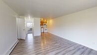 This 2-bedroom, 1-bathroom unit offers a practical and efficient single-floor layout. The open living area is bright and clean, featuring light wood-style vinyl flooring throughout and crisp white walls that maximize the sense of space. A sliding glass door floods the living room with natural light and provides direct views of a green outdoor area, complemented by vertical blinds and a wall-mounted AC unit for year-round comfort.

The kitchen is efficiently arranged with warm honey-toned wood cabinetry, laminate countertops, and a full suite of white appliances including a range, over-the-range microwave, dishwasher, and refrigerator, along with a stainless steel sink.

The primary bedroom is generously sized and features soft carpeting, a wall-mounted AC unit, a large window for natural light, and a dedicated closet. The second bedroom also offers carpeted flooring and includes built-in closet storage. Both rooms maintain a clean, neutral aesthetic throughout.

The bathroom features a full tub-shower combination with white tile surround. A connecting hallway provides organized access to all rooms. Baseboard heating is present throughout, ensuring consistent warmth. The overall ambiance is clean, functional, and move-in ready.