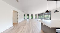 This thoughtfully designed 3-bedroom, 3-bathroom residence at The Mill delivers a seamless blend of modern architecture and comfortable living across a generous single-floor layout. Light-toned hardwood flooring flows throughout, unifying each space with a clean, cohesive aesthetic.

The expansive open-concept living and dining area serves as the heart of the home, bathed in natural light through a series of floor-to-ceiling black-framed windows fitted with roller shades. The lush greenery and water views visible through the glass create a serene indoor-outdoor connection, further enhanced by direct balcony access.

The contemporary kitchen features a large central island with a white quartz countertop, dark cabinetry, stainless steel appliances, a gas range, and pendant lighting—offering both style and function. A tiled backsplash and under-cabinet range hood complete the culinary space.

A long, bright hallway with recessed lighting connects the private bedroom wing. Each bedroom is well-proportioned with large windows framing outdoor views and ceiling fans for comfort. The primary suite includes a custom-built walk-in closet with shelving, hanging rods, and integrated drawer storage.

The bathrooms are finished in a clean, modern style with large-format tile flooring, floating vanities, white countertops, and matte black hardware accents throughout.