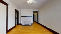 Located at 3049 N Maryland Ave in Milwaukee's vibrant 53211 neighborhood, this single-floor residence blends classic architectural character with thoughtful updates. Warm hardwood floors run throughout the living spaces, complemented by rich dark wood trim, door casings, and baseboards that define the home's craftsman-era aesthetic.

The living room serves as the centerpiece of the space, featuring a white-tiled decorative fireplace with a dark wood mantel, crown molding, and a ceiling fan — a comfortable and characterful gathering area. Adjacent rooms continue the cohesive design, with multiple bedrooms offering natural light through double-hung windows, ceiling fans, and classic cast-iron radiators that speak to the home's heritage heating system.

Storage is well-considered, with at least one closet fitted with built-in shelving behind a handsome original five-panel wood door with vintage hardware. One room features a distinctive bay window configuration, flooding the space with additional natural light.

The kitchen presents a clean, updated aesthetic with white shaker-style cabinetry, dark granite-look countertops, a stainless steel sink, black hardware, and a herringbone-patterned tile backsplash, all set atop light marble-style flooring. The overall layout flows efficiently, making this a well-preserved and functional Milwaukee residence.
