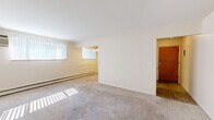 This single-floor residence at 775 Wagner Dr in Battle Creek, Michigan offers a clean, functional layout with a bright and neutral aesthetic throughout. The spacious living area is finished with plush wall-to-wall carpeting and features large windows dressed with vertical blinds, allowing generous natural light to fill the room. Baseboard heating runs along the walls, providing efficient climate control. The living space flows openly into a secondary area, also carpeted, offering flexibility for dining or additional seating arrangements. The bedroom is a well-proportioned, carpeted room equipped with a ceiling fan and a window with vertical blinds, maintaining the home's consistent light and airy feel, along with its own baseboard heating. The kitchen features warm wood-toned cabinetry, wood-look flooring, and includes a full suite of appliances — a refrigerator, electric coil range, over-the-range microwave, and a dishwasher. A hallway connects the kitchen to adjacent spaces, enhancing the flow of the floorplan. The bathroom is appointed with white tile flooring, a full tub-shower combination with a white surround, and includes a toilet and vanity. Throughout the space, the neutral color palette, consistent finishes, and practical layout make this a comfortable and move-in-ready home.