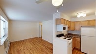 This single-floor space offers a practical and well-organized layout designed for comfortable everyday living. The open-concept floor plan seamlessly connects the kitchen and living area, creating a sense of spaciousness and ease of movement throughout the unit. Warm hardwood flooring runs consistently across the main living spaces, adding a natural and inviting quality to the interior.

The kitchen is efficiently arranged and features light wood cabinetry that provides ample storage, dark countertops, a white electric range, an over-the-range microwave, and a double-basin sink. A peninsula-style counter defines the boundary between the kitchen and the open living area, offering both workspace and a casual dining or prep surface.

The living area is bright and open, with clean white walls and a ceiling fan that contributes to airflow and comfort. The neutral color palette throughout the space provides a versatile backdrop suitable for a variety of furnishing styles. A hallway visible from the main area leads to additional rooms, suggesting a functional separation of living and private spaces. Overall, the space presents a clean, move-in-ready environment with a straightforward and efficient design.