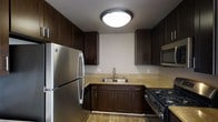This single-floor residence offers a thoughtfully designed living space with a kitchen that serves as a functional centerpiece. The kitchen is outfitted with rich, dark espresso-toned cabinetry that extends to the ceiling, providing generous storage throughout. Light granite-style countertops offer a pleasing contrast to the dark cabinets, creating a balanced and visually appealing workspace. Stainless steel appliances, including a full-size refrigerator, a built-in microwave, and a gas range, lend a modern and practical edge to the space. A double-basin stainless steel sink with a sleek brushed nickel faucet is positioned beneath a neutral wall, making it a clean and efficient workstation. Warm hardwood-style flooring runs through the kitchen, adding a touch of natural warmth to the overall aesthetic. A flush-mount ceiling light provides bright, even illumination throughout the kitchen. The textured ceiling adds a subtle architectural detail. Overall, the space combines dark, warm tones with modern fixtures to create a cohesive, functional, and inviting environment suited for everyday living.