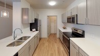 Located on Bradley Park Lane in Cumming, Georgia, this single-story residence offers a thoughtfully designed layout with modern finishes and a clean, contemporary aesthetic. The open floor plan is visible from an aerial view, revealing distinct living, dining, kitchen, bedroom, and utility zones arranged for both comfort and practicality.

The living room features crown molding, wood-look flooring, and large windows that invite natural light and outdoor views, creating a bright and welcoming atmosphere. A comfortable seating arrangement anchors the space, complemented by neutral tones throughout.

The adjacent dining area is defined by a striking spherical chandelier with exposed bulbs, crown molding, and light wood flooring. Framed artwork lines the walls, adding a refined touch to the space.

The galley-style kitchen is equipped with stainless steel appliances, light gray cabinetry, white countertops, and wood-look flooring, offering ample storage and a clean, functional workspace. A dedicated laundry room with full-size washer and dryer adds everyday convenience.

The bedrooms are carpeted and generously sized, with one featuring a walk-in closet. The bathrooms are finished with white surrounds, soaking tub-shower combos, and modern vanities with white countertops.