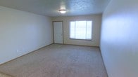 This two-floor space presents a straightforward and functional design with neutral tones throughout. The pictured main room features wall-to-wall carpeting in a light beige tone, providing a comfortable and understated foundation for the space. Walls are finished in a soft, neutral hue, complementing the overall clean aesthetic. A flush-mount ceiling light fixture provides overhead illumination, while a textured ceiling adds subtle visual interest. A large window allows natural light to fill the room, creating a bright and open atmosphere. Warm wood-toned baseboards frame the perimeter of the room, adding a modest architectural detail that ties the space together. A white interior door with matching trim provides access to an adjoining area, maintaining a cohesive and consistent design language throughout. The room's generous proportions offer ample flexibility for a variety of furnishing arrangements. The overall ambiance is clean, neutral, and practical, making it a versatile space well-suited to a range of uses. With two floors in total, the layout provides separation between living areas, offering additional functionality and privacy throughout the property.