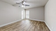 This single-story, one-bedroom, one-bathroom unit is located at 19606 Park Row Dr in Houston, TX 77084. Wood-look plank flooring runs consistently throughout all rooms, providing a cohesive and easy-to-maintain finish. Neutral-toned walls and white trim create a clean, bright backdrop across the space.

The open-concept kitchen and living area form the heart of the unit. The kitchen features dark cabinetry contrasted by light granite-style countertops, a white tile backsplash, and stainless steel appliances including a refrigerator and dishwasher. The living area benefits from natural light and is accessed via a sliding glass door that opens to a private balcony.

The bedroom is a comfortable size, equipped with a ceiling fan with light fixture, and windows fitted with blinds. A dedicated closet provides built-in storage. The bathroom is positioned adjacent to the bedroom and includes a vanity with dark cabinetry, a lighted mirror, and a full tub-shower combination with tiled walls. Textured ceilings are present throughout the unit, and HVAC venting is visible in the bedroom area.