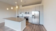 Located at 1830 Cadiz St in Dallas, TX, this single-floor unit showcases a clean, contemporary design with a neutral color palette and wood-style flooring that flows consistently throughout the main living areas. The open-concept layout connects the living area and kitchen seamlessly, creating a spacious, functional environment ideal for everyday living and entertaining.

The kitchen is a standout feature, equipped with stainless steel appliances including a range, microwave, refrigerator with ice and water dispenser, and dishwasher. Flat-front cabinetry in a soft gray-beige tone extends to the ceiling, maximizing storage. A white subway tile backsplash, undermount stainless steel sink with a matte black faucet, and a quartz-topped island with pendant lighting above complete the well-appointed space.

The living area benefits from natural light through multiple windows fitted with blinds, and ceiling fans provide additional comfort. Recessed lighting and pendant fixtures add to the modern ambiance throughout.

The bedroom features plush carpet flooring and a neutral finish, offering a quiet, comfortable retreat. The bathroom includes a vanity with quartz countertop, wood-style tile flooring, and a glass-enclosed walk-in shower with elegant marble-look tile surround. Overall, the space presents a polished, move-in-ready aesthetic.