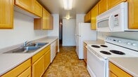 Located at 2701 AL Ogdon Way in Cheney, Washington, this single-floor unit offers a practical and comfortable layout designed for everyday living. The galley-style kitchen is well-appointed with warm wood cabinetry, light countertops, a double basin sink, a dishwasher, electric range, refrigerator, and over-the-range microwave. Tile flooring runs throughout the kitchen, transitioning into a bright dining area illuminated by a pendant light fixture and a large window that invites natural light. The expansive living room features plush wall-to-wall carpeting, a baseboard heating system, multiple windows, and a sliding glass door that opens directly to an outdoor area, creating a seamless indoor-outdoor connection. Two bedrooms are carpeted and naturally lit through gridded windows, with one bedroom offering a sliding closet with built-in shelving. Two bathrooms serve the unit, each finished with warm tile flooring and wood-toned vanity cabinetry — one with a walk-in shower stall and the other with a full shower/tub combination. Throughout the unit, neutral wall tones and clean finishes create a bright, functional living environment.