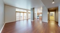 This single-floor residence offers a thoughtfully designed layout that balances open communal spaces with private retreats. The expansive living area is a standout feature, showcasing rich hardwood flooring, a structural column accent, and a wall of large windows with slatted blinds that invite abundant natural light and provide views of the surrounding exterior. A balcony is accessible from the living space, extending the area outdoors.

The kitchen is well-equipped and efficiently arranged in an L-shaped configuration, featuring warm honey-toned cabinetry that extends to notable heights, granite countertops, a stainless steel refrigerator, electric range, and built-in microwave. A sink with additional counter space completes the functional layout.

The bedrooms are finished with plush carpeting and neutral gray walls, with windows providing natural light. One bedroom benefits from direct access to a generously sized walk-in closet outfitted with wire shelving systems for organized storage.

The bathrooms maintain a clean, bright aesthetic with white cabinetry, granite vanity tops, large mirrors, and soaking tubs with assist bars. Light tile flooring ties the spaces together cohesively throughout.