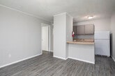 Located at 616 Folmar St in Troy, Alabama, this single-story unit offers a functional and straightforward layout designed for efficient everyday living. The main living area is open and well-proportioned, featuring durable wood-look vinyl plank flooring that runs consistently throughout the space, neutral gray walls, and a textured ceiling. A wall-mounted HVAC unit provides climate control, and a window allows natural light to brighten the room alongside a front entry door.

The kitchen is positioned along one side of the open floor plan and is separated from the living area by a peninsula counter finished with a light wood-tone laminate surface, offering additional prep space and a casual dining or bar-style seating option. Upper cabinetry in a muted taupe finish provides storage, complemented by a built-in sink and a full-size refrigerator. A fire extinguisher is also visibly mounted for safety.

A hallway connects the living and kitchen areas to the additional rooms, including a bedroom that offers a calm, neutral environment with matching flooring and a textured ceiling. The bathroom is clean and simply appointed, featuring a white vanity with under-cabinet storage, a white countertop with chrome fixtures, a medicine cabinet with mirror, and overhead vanity lighting. The overall aesthetic is clean, practical, and move-in ready.