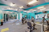 Located at 151 Grande View Dr in Biloxi, Mississippi, this single-floor fitness center delivers a well-equipped and energizing workout environment with a distinctly coastal aesthetic. The space is defined by bold teal accent walls that create a vibrant, motivating atmosphere, complemented by a dramatic floor-to-ceiling ocean wave mural that serves as a striking focal point and reinforces the Gulf Coast character of the facility.

The layout is open and generously proportioned, allowing for comfortable movement between equipment zones. Full-length mirrors line key sections of the walls, visually expanding the space and providing users with form-checking capability throughout their workouts. Overhead, vaulted ceiling sections are fitted with ceiling fans and recessed fluorescent lighting, ensuring the room remains well-lit and well-ventilated.

The cardio zone is outfitted with treadmills, upright and recumbent Matrix bikes, and a spinning bike, positioned near large windows that provide natural light and views of the surrounding palm-lined outdoor area. The strength training area includes a cable machine, weight bench, free weights, and additional resistance equipment. A wall-mounted television, a water fountain, and designated floor markers for stretching or mat work round out the amenities, making this a fully functional fitness facility.