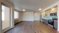 Located at 950 W 17th Ave in Junction City, Oregon, this well-designed single-floor residence offers a clean, contemporary aesthetic throughout. The open-concept living and dining area is anchored by rich, dark hardwood-style flooring that extends seamlessly throughout the main living spaces, creating a warm and cohesive atmosphere. Multiple windows dressed with vertical blinds allow abundant natural light to fill the room, while a wall-mounted HVAC unit and a private exterior door add practical convenience. The kitchen is a standout feature, showcasing two-tone cabinetry with light wood upper cabinets and slate-blue lower cabinets, a teal glass tile backsplash, light countertops, and a full suite of stainless steel appliances including a refrigerator, range, over-the-range microwave, and dishwasher. Recessed lighting illuminates the kitchen area effectively. The two bedrooms are finished with plush wall-to-wall carpeting and each include windows with vertical blinds that bring in natural light. The bathroom is outfitted with a full soaking tub and shower combination, a toilet, and an overhead cabinet for storage. The overall design is modern, clean, and move-in ready.