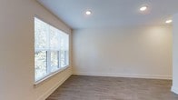 This single-floor residence features a 1-bedroom, 1-bathroom layout designed to maximize comfort and functionality. The interior showcases a modern aesthetic with neutral, warm-toned walls that create a bright and welcoming atmosphere throughout. Durable wood-look plank flooring runs throughout the space, offering both style and easy maintenance. Recessed lighting provides consistent illumination, complementing the natural light that fills the rooms. The bedroom is generously proportioned, featuring a large window dressed with horizontal blinds that frame lush outdoor greenery, filling the room with soft, natural light and providing a pleasant connection to the surrounding landscape. Clean white baseboards and smooth walls contribute to the overall crisp, contemporary feel of the space. The layout is thoughtfully designed for single-floor living, ensuring seamless flow between rooms. The neutral color palette and modern finishes make this residence a versatile and move-in ready home, well-suited for a variety of personal styles and furnishing preferences.
