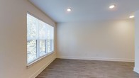 This single-floor residence features a 1-bedroom, 1-bathroom layout designed to maximize comfort and functionality. The interior showcases a modern aesthetic with neutral, warm-toned walls that create a bright and welcoming atmosphere throughout. Durable wood-look plank flooring runs throughout the space, offering both style and easy maintenance. Recessed lighting provides consistent illumination, complementing the natural light that fills the rooms. The bedroom is generously proportioned, featuring a large window dressed with horizontal blinds that frame lush outdoor greenery, filling the room with soft, natural light and providing a pleasant connection to the surrounding landscape. Clean white baseboards and smooth walls contribute to the overall crisp, contemporary feel of the space. The layout is thoughtfully designed for single-floor living, ensuring seamless flow between rooms. The neutral color palette and modern finishes make this residence a versatile and move-in ready home, well-suited for a variety of personal styles and furnishing preferences.