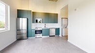 Located at 315 NW 32nd Street in Miami, FL, this modern one-bedroom, one-bathroom unit offers a thoughtfully designed layout across a single floor. The space features soaring ceilings with exposed concrete detailing, large-format grey tile flooring throughout, and crisp white walls that create a bright, airy atmosphere.

The kitchen is a standout, outfitted with matte teal cabinetry, a white tile backsplash, and a full suite of stainless steel appliances including a refrigerator, range, and dishwasher. A stacked washer and dryer unit is conveniently integrated into the kitchen area.

The spacious bedroom benefits from generous natural light through sliding windows that frame lush green tree views, reinforcing a sense of openness and calm. The room also includes a built-in open closet system with shelving and hanging rods, as well as a dedicated desk nook — ideal for organized, functional living.

The bathroom is clean and contemporary, featuring large-format white tile, a walk-in shower with a window for natural light, matte black fixtures, and a sleek navy floating vanity. The overall design aesthetic is minimalist and modern, with cohesive finishes throughout that reflect Miami's contemporary architectural sensibility.