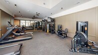 Located at 382 Red Bud Cir in Hendersonville, NC, this fitness facility offers a comprehensive and thoughtfully designed exercise space on a single floor. The room is generously proportioned, providing ample space for a wide variety of workout disciplines without feeling crowded.

The cardio zone features a row of TRUE brand treadmills positioned along floor-to-ceiling windows that allow natural light to pour in and offer views of the surrounding greenery. Ceiling fans overhead help maintain airflow throughout the space. The strength training area is equally well-appointed, with a multi-station cable machine, a dumbbell rack with a full mirror wall, a weight bench, and an assortment of kettlebells and medicine balls neatly organized on a dedicated rack.

A standout feature of the facility is the Freedom Climber — an interactive climbing wall that adds a unique, functional training element rarely found in fitness spaces of this scale. Additional cardio equipment includes stationary bikes and a rowing machine, rounding out the options for a full-body workout.

The flooring throughout is durable rubberized gym matting, providing safety and comfort underfoot. Neutral warm tones on the walls, recessed and track lighting, and a clean, uncluttered layout give the space a polished, professional aesthetic. The overall ambiance is energizing yet refined, making it a versatile and high-quality fitness environment.