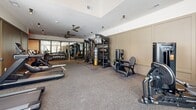 Located at 382 Red Bud Cir in Hendersonville, NC, this fitness facility offers a comprehensive and thoughtfully designed exercise space on a single floor. The room is generously proportioned, providing ample space for a wide variety of workout disciplines without feeling crowded.

The cardio zone features a row of TRUE brand treadmills positioned along floor-to-ceiling windows that allow natural light to pour in and offer views of the surrounding greenery. Ceiling fans overhead help maintain airflow throughout the space. The strength training area is equally well-appointed, with a multi-station cable machine, a dumbbell rack with a full mirror wall, a weight bench, and an assortment of kettlebells and medicine balls neatly organized on a dedicated rack.

A standout feature of the facility is the Freedom Climber — an interactive climbing wall that adds a unique, functional training element rarely found in fitness spaces of this scale. Additional cardio equipment includes stationary bikes and a rowing machine, rounding out the options for a full-body workout.

The flooring throughout is durable rubberized gym matting, providing safety and comfort underfoot. Neutral warm tones on the walls, recessed and track lighting, and a clean, uncluttered layout give the space a polished, professional aesthetic. The overall ambiance is energizing yet refined, making it a versatile and high-quality fitness environment.