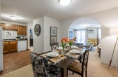 This single-floor residence offers a thoughtfully designed layout that connects the key living spaces in a natural, functional flow. The open-concept living and dining area serves as the heart of the home, where a graceful arched entryway separates the two zones while maintaining a sense of openness. The dining area accommodates a full-sized table and is finished with neutral carpet and flush ceiling lighting. The adjacent living room features sliding glass doors that invite natural light and provide outdoor access, complemented by a wall-mounted television area and baseboard heating throughout.

The kitchen is equipped with warm wood-toned cabinetry, dark countertops, and a full suite of white appliances including a refrigerator, range, built-in microwave, and dishwasher. Wood-style flooring adds a practical, clean aesthetic to the space.

Two carpeted bedrooms offer comfortable retreats, each with generous windows dressed with curtain panels that provide privacy and light control. The primary bedroom features a large window and ample space for a full bedroom suite.

The bathroom includes a tub-shower combination, vanity with under-sink storage, and wood-style flooring, maintaining a consistent finish with the rest of the home. Textured ceilings are present throughout, giving the space a classic residential character.