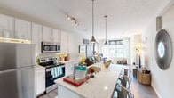 Located on North High Street in Columbus, Ohio, this modern 2-bedroom, 2-bathroom residence offers a well-designed open-concept layout across a single floor. The kitchen is a standout feature, showcasing white cabinetry, granite countertops, stainless steel appliances including a refrigerator, range, and microwave, and a large center island with pendant lighting and bar seating — flowing seamlessly into the living area. The living room is bright and welcoming, filled with natural light through oversized windows that frame views of the vibrant Columbus streetscape. Wood-style flooring runs throughout the main living areas, adding warmth and continuity. The primary bedroom features expansive floor-to-ceiling windows offering striking urban views, plush carpeting, and a closet for storage. The second bedroom is equally comfortable, with carpeted floors and a reach-in closet. Both bathrooms are finished with clean, modern fixtures, vanities with white countertops, and wood-style flooring. A dedicated utility room and additional closet provide practical storage solutions. The overall ambiance is contemporary and urban, combining functional design with stylish finishes suited for city living in one of Columbus's most walkable neighborhoods.