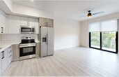 Located at 18412 Homestead Ave in Miami, FL, this thoughtfully designed three-bedroom, two-bathroom unit offers a clean, modern aesthetic throughout its efficiently utilized single-floor layout. Light wood-style flooring flows seamlessly across all living areas, complementing the bright white walls and creating a cohesive, airy atmosphere.

The kitchen is a standout feature, equipped with stainless steel appliances including a French door refrigerator, range, microwave, and dishwasher. Two-tone cabinetry — white upper cabinets paired with natural wood-tone lower cabinets — is accented by white subway tile backsplash and black hardware, lending a contemporary feel. The kitchen opens directly into the living area, enhancing the sense of openness.

The primary bedroom includes a ceiling fan, access to a private balcony with lush green views, and a spacious closet. The two additional bedrooms each feature large windows with roller shades, filling the rooms with natural light and offering pleasant outdoor views. Both bathrooms are finished with neutral tile, white quartz countertops, and grey cabinetry with black hardware; one includes a glass-enclosed walk-in shower, while the other offers a full tub-shower combination. A connecting hallway ties all rooms together efficiently.