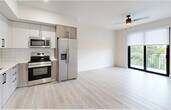 Located at 18412 Homestead Ave in Miami, FL, this thoughtfully designed three-bedroom, two-bathroom unit offers a clean, modern aesthetic throughout its efficiently utilized single-floor layout. Light wood-style flooring flows seamlessly across all living areas, complementing the bright white walls and creating a cohesive, airy atmosphere.

The kitchen is a standout feature, equipped with stainless steel appliances including a French door refrigerator, range, microwave, and dishwasher. Two-tone cabinetry — white upper cabinets paired with natural wood-tone lower cabinets — is accented by white subway tile backsplash and black hardware, lending a contemporary feel. The kitchen opens directly into the living area, enhancing the sense of openness.

The primary bedroom includes a ceiling fan, access to a private balcony with lush green views, and a spacious closet. The two additional bedrooms each feature large windows with roller shades, filling the rooms with natural light and offering pleasant outdoor views. Both bathrooms are finished with neutral tile, white quartz countertops, and grey cabinetry with black hardware; one includes a glass-enclosed walk-in shower, while the other offers a full tub-shower combination. A connecting hallway ties all rooms together efficiently.